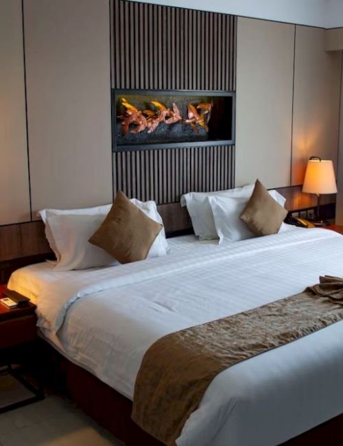 A modern hotel room features a king-sized bed with white linens, bedside tables with lamps, and a decorative wall panel behind the bed.