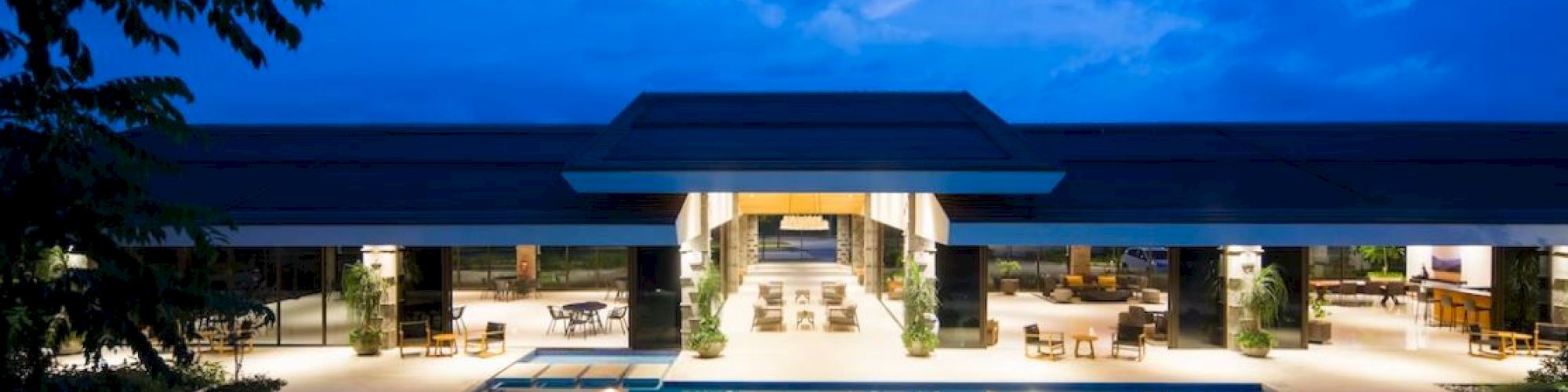 A luxurious building with an illuminated swimming pool at dusk, featuring open seating areas and modern architectural design elements.