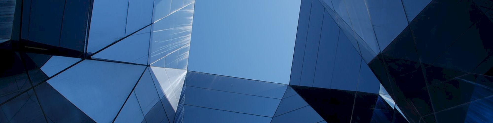 The image displays a geometric architectural design composed of reflective glass panels, creating a dynamic visual effect with the sky visible in the center.