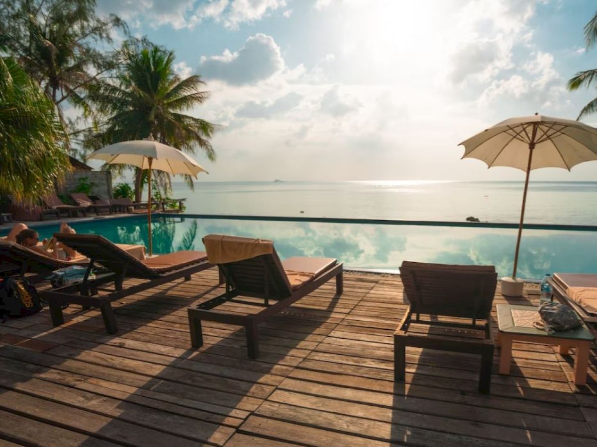 A serene poolside scene with lounge chairs and umbrellas overlooking a calm sea, surrounded by palm trees and bathed in soft sunlight.