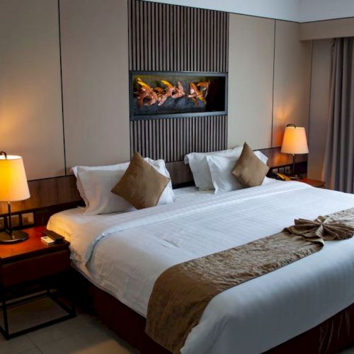 A neatly arranged hotel room with a double bed, bedside tables, lamps, and a wall-mounted decorative art piece above the bed, ending the sentence.