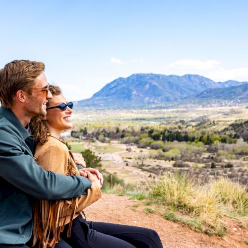 Two people sit together, embracing, while enjoying a scenic mountain view in an outdoor setting during daytime.
