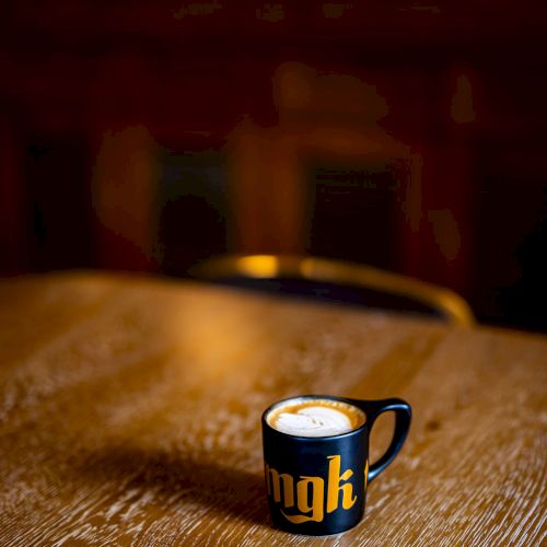 A small black coffee cup with a design on it sits on a wooden table in a dimly lit room.
