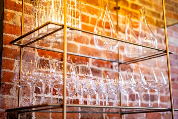 The image shows shelves mounted on a brick wall, holding a collection of various glassware including wine glasses and decanters.