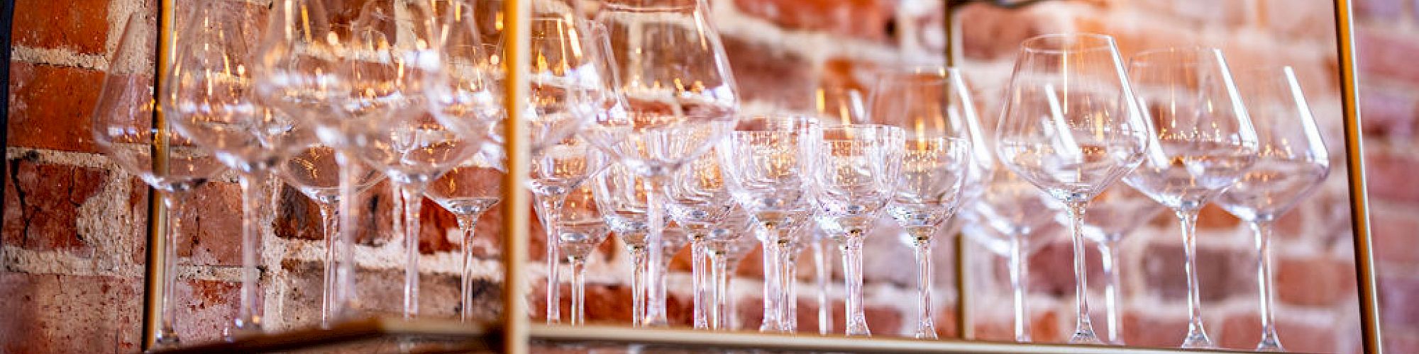 The image shows shelves with an assortment of glassware, including wine glasses and decanters, against a backdrop of a brick wall.
