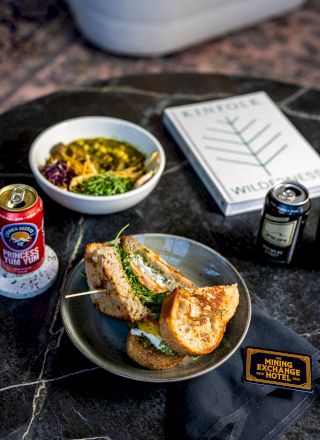 The image shows a meal with a sandwich on a plate, a bowl of food, a book titled 