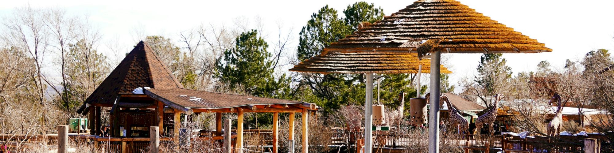The image shows a rustic outdoor setting with wooden structures, triangular and pyramid-shaped roofs, and a snowy landscape.