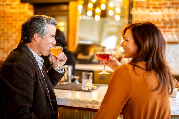 A man and a woman are sitting at a bar, enjoying drinks and smiling at each other.