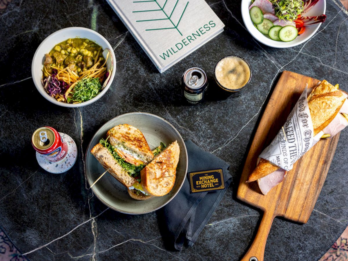A table with various foods including sandwiches, salad, a can of drink, a latte, and a book labeled 