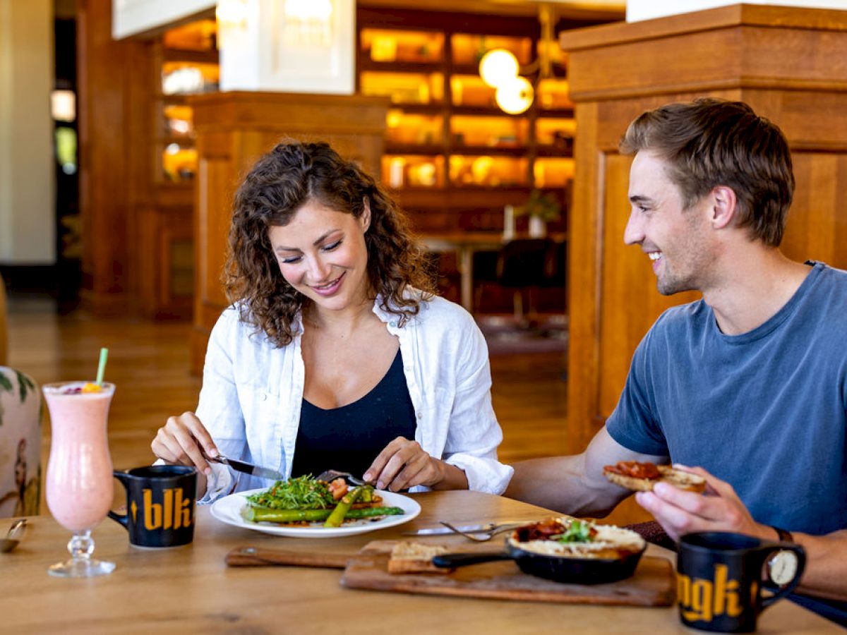 A man and woman are dining together, enjoying a meal with drinks at a wooden table in a cozy setting.