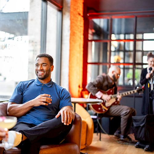 Two people are enjoying drinks in a lounge with live guitar music in the background.