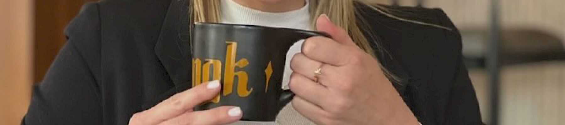 A person is smiling and holding a black mug with the word