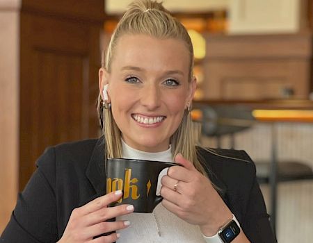 A person is smiling and holding a black mug with the word 