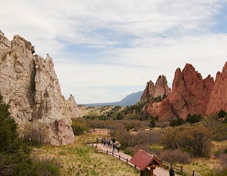 The image shows a scenic landscape with sandstone rock formations, a walking path, some people, and a distant mountain under a partly cloudy sky.