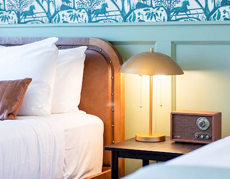 A cozy bedroom scene with two beds, a vintage radio, and a modern lamp on a nightstand, with a green and blue patterned wallpaper.