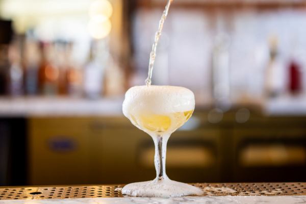 A glass overflowing with foam while being filled with a beverage, likely beer, on a bar counter.