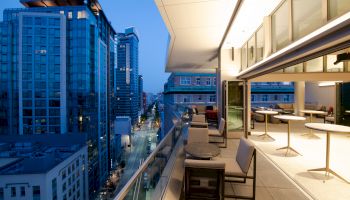 A modern cityscape view from a balcony at dusk, featuring a luxurious outdoor seating area and glass buildings in the background, creating a serene ambiance.