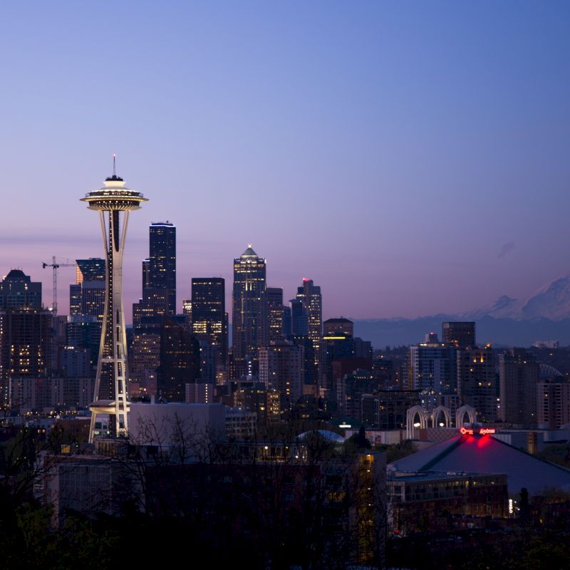 The image shows a city skyline at dusk with the Space Needle prominently featured, and a distant mountain in the background.