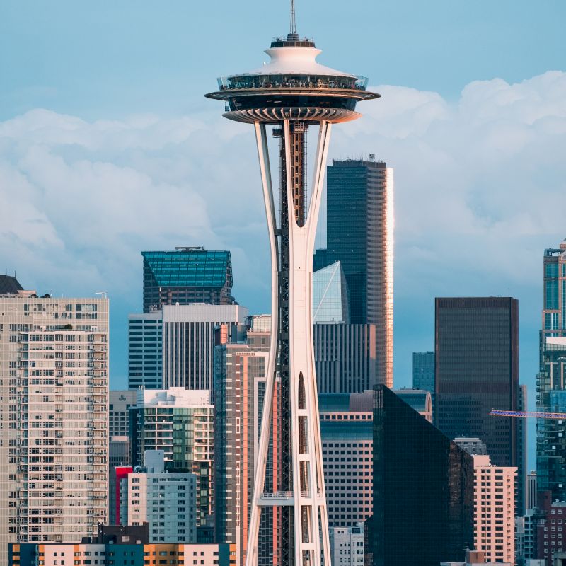 The image shows a cityscape featuring the Space Needle with several skyscrapers in the background under a partly cloudy sky.