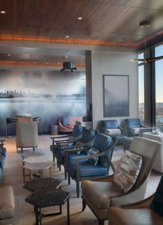 A modern lounge with multiple cushioned chairs, tables, large windows offering a scenic view of a Ferris wheel and waterfront, and wall art.
