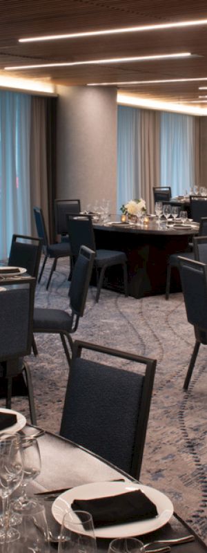 This image shows a modern, elegantly set dining or banquet room with round tables covered in black tablecloths, silverware, and centerpieces, ready for an event.