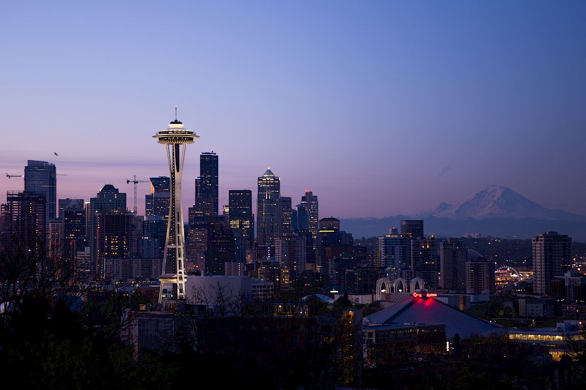This image shows the Seattle skyline at dusk, with the Space Needle prominently visible and Mount Rainier in the background.